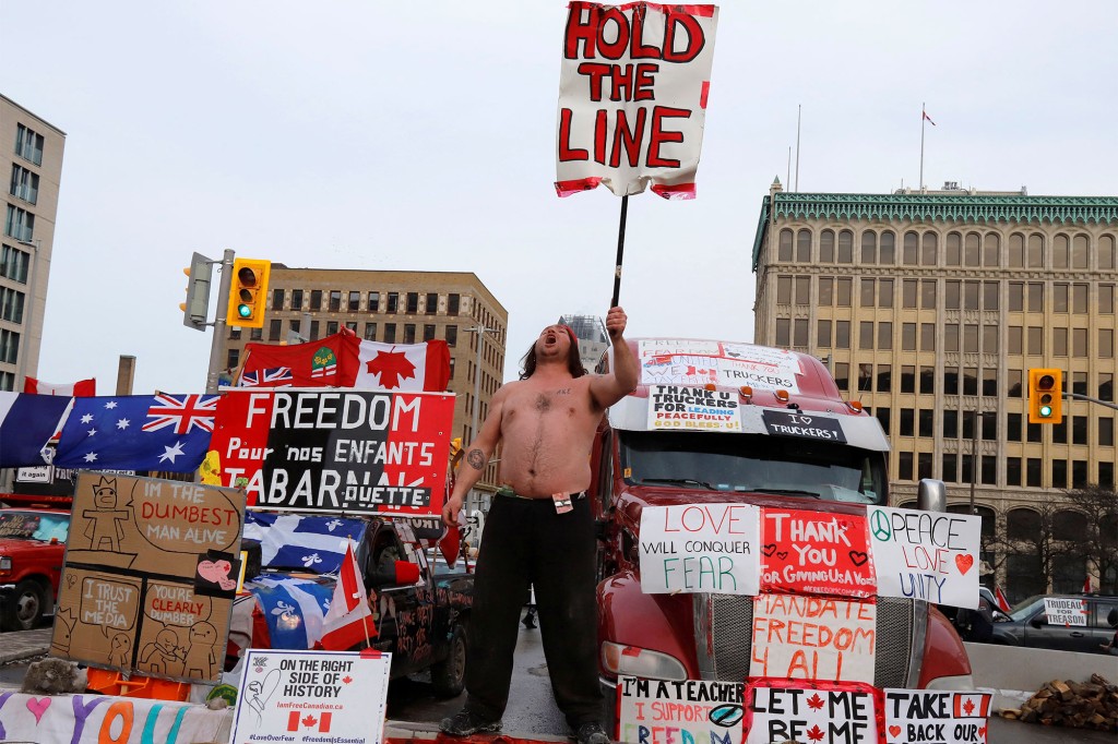 A person holds a sign in front of trucks blocking a downtown street as truck drivers and their supporters continue to protest against mandates for a coronavirus (COVID-19) vaccine in Ottawa, Ontario, Canada.