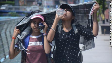 Two young girls cover their heads as they walk and drink water in the scorching afternoon heat in Mumbai, India.