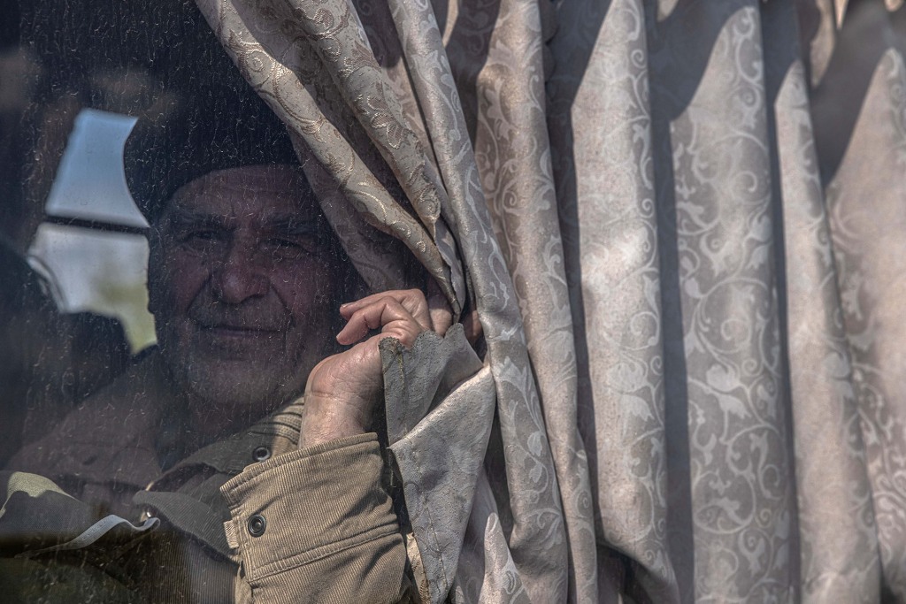 An elderly man looks at him as he sits on a bus after arriving from the frontline town of Urekiev, at the evacuation point in Zaporizhia, Ukraine