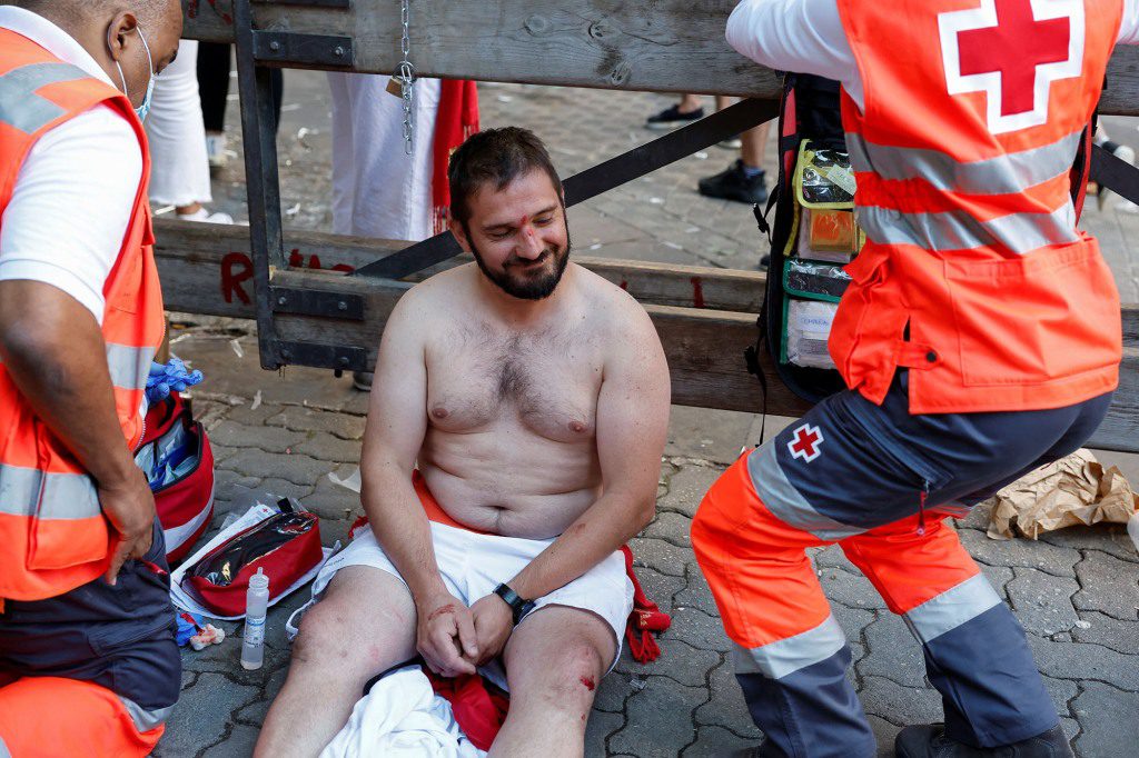 A shirtless runner smiles despite needing treatment for his injuries.