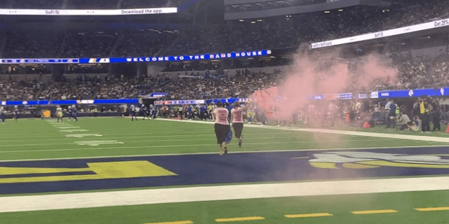 Two women dash into the SoFi stadium with smoke flares to highlight the upcoming experience.